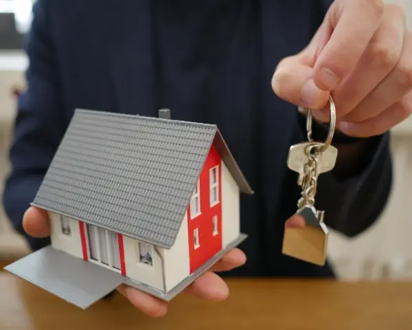 Mano ofrece maqueta de casa y llaves, símbolo de propiedad y seguridad ante la ley antiokupas.