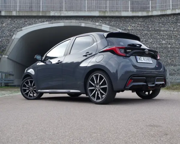 Szary Toyota Yaris GR Sport z czarnym spojlerem i dyfuzorem, zaparkowany przed tunelem.