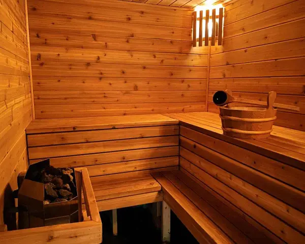 Drewniana sauna z kamieniami i wiadrem. Inspiracja, jak zbudować saunę, by cieszyć się relaksem.