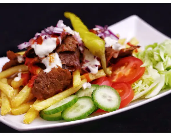 En tallrik med kebab, pommes frites, tomater, gurka, sallad och en grön chili. Perfekt för att inspireras till ett gott kebabsås recept.