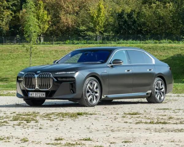 Elegancki, grafitowy BMW 740d na tle zieleni. Luksusowa limuzyna prezentuje się imponująco.