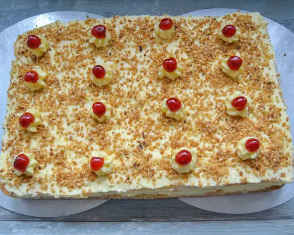 Rechteckiger Frankfurter Kranz Kuchen, bestreut mit gehackten Nüssen und verziert mit Sahnetuffs und Kirschen. Sally liebt diese Schnitten!