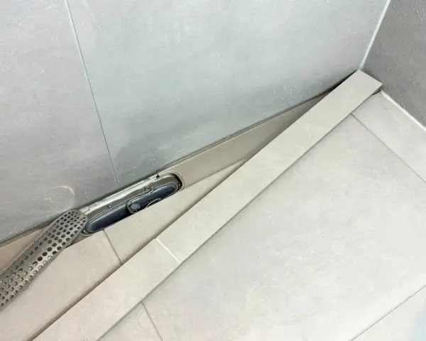 En dusch med en Purus vakuumventil och ett perforerat galler. Vatten droppar på de ljusa kakelplattorna.