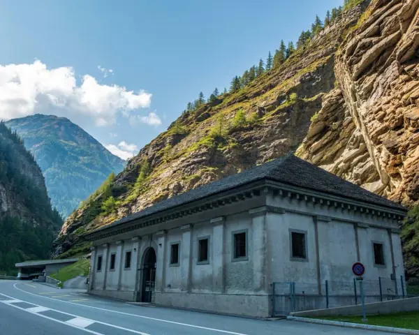 Edificio in pietra ai piedi di una montagna rocciosa, con strada e tunnel. Un passo alpino che sembra non finire mai, un vero sempione passo.