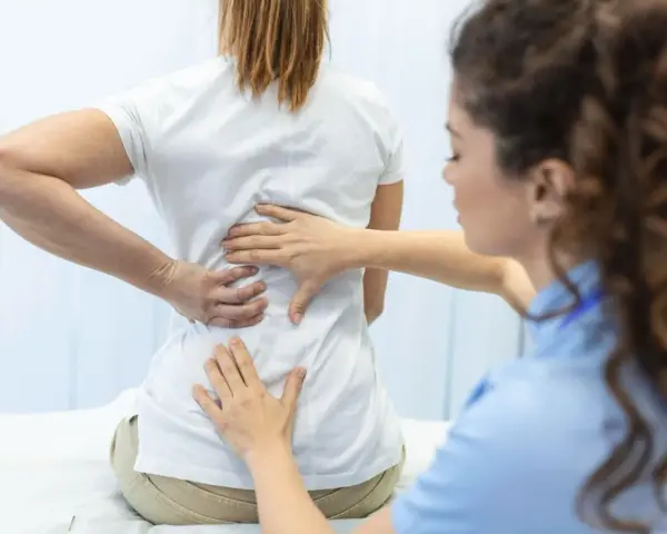 Fizjoterapeuta bada plecy pacjentki. Po długiej rehabilitacji wreszcie wyleczyłem kręgozmyk i czuję się znacznie lepiej.