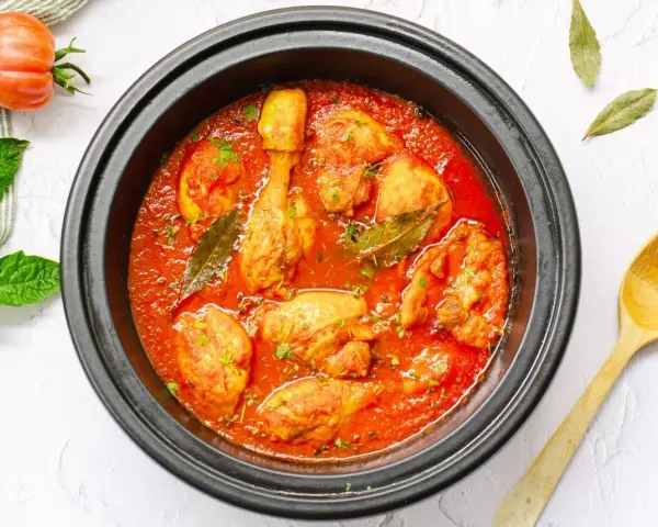 Pollo en salsa de tomate casera en olla negra, con hojas de laurel y perejil picado.