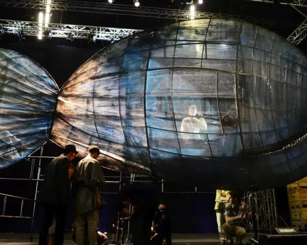 Scena teatralna z wielką, szklaną rybą, w której siedzi człowiek. To może być cud Jonasza.