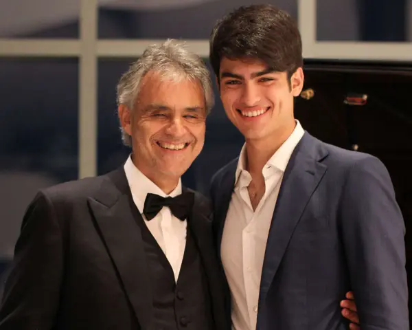 Andrea Bocelli młody i jego syn Matteo, obaj uśmiechnięci, w eleganckich strojach.