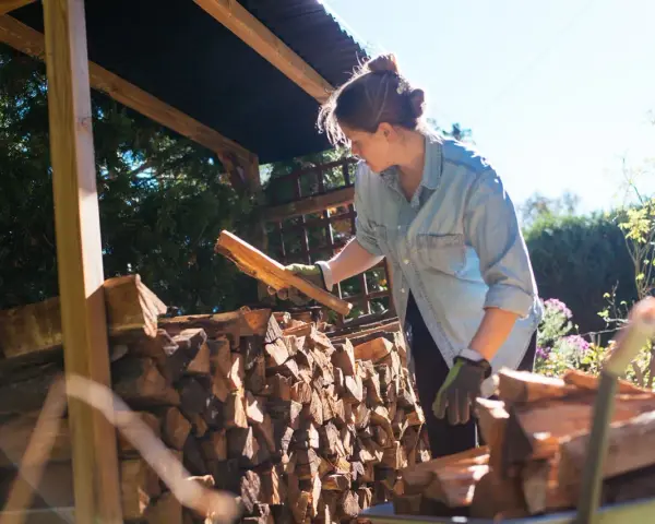 Femme avec des bûches de bois sous un abri.
