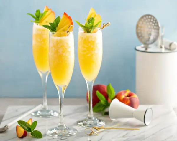 Orzeźwiający drink z prosecco i sokiem pomarańczowym, udekorowany brzoskwinią i miętą. Idealny na letnie popołudnie.