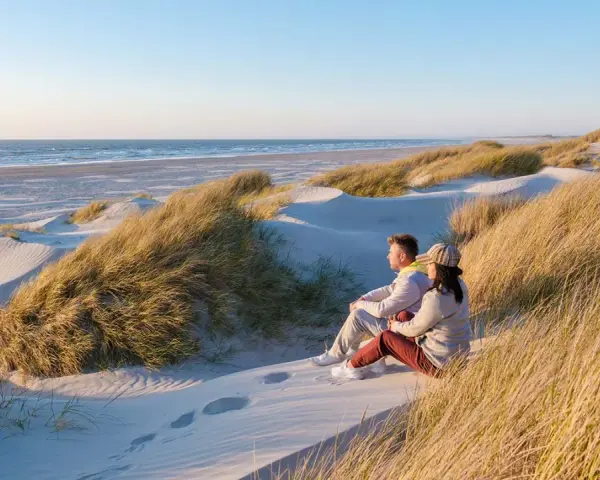 Ett par sitter på en sanddyn och njuter av utsikten över havet. Vackra sanddyner med gräs sträcker sig längs kusten, en idyllisk plats i en nationalpark i Danmark.