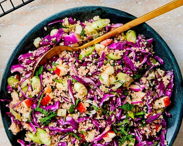 En färgstark couscous sallad med rödkål, äpple och färska örter. En gyllene sked vilar i den fräscha salladen.