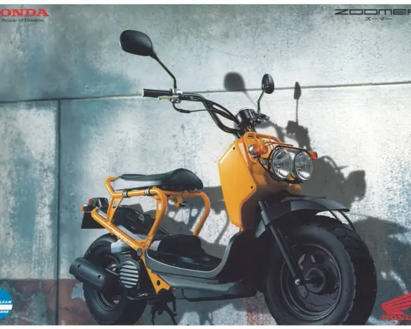 Pomarańczowy Honda Zoomer z podwójnymi reflektorami i charakterystyczną ramą, gotowy do miejskich przygód.