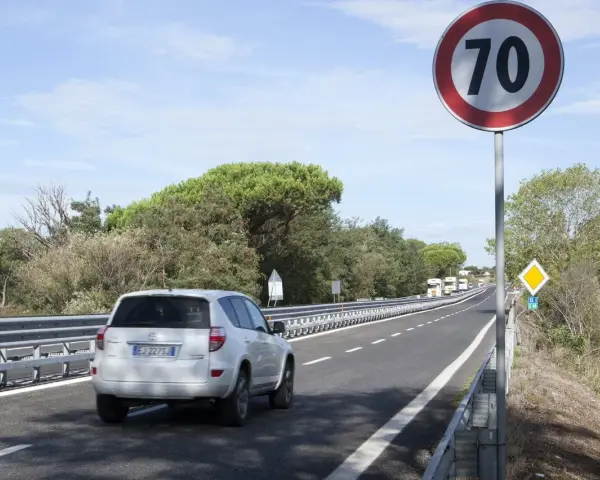 Un'auto bianca percorre una strada extraurbana secondaria, superando un cartello di limite di velocità a 70 km/h.