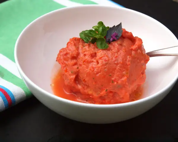Ein erfrischendes Tomaten-Eis, garniert mit Basilikum, in einer weißen Schüssel.