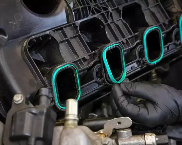 A gloved hand installs a new intake manifold gasket, ensuring a tight seal for optimal engine performance.