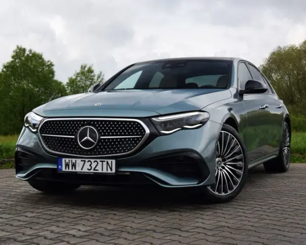 Elegancki Mercedes E220d w kolorze miętowym, zaparkowany na brukowanej nawierzchni, z zielenią w tle.