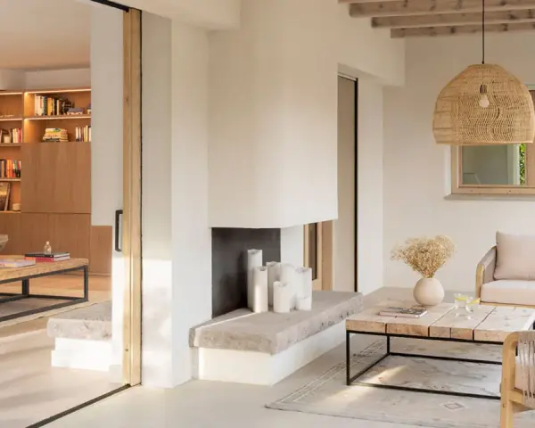 Salón luminoso con chimenea de piedra, muebles de madera y textiles naturales, evocando un relajante estilo ibicenco.