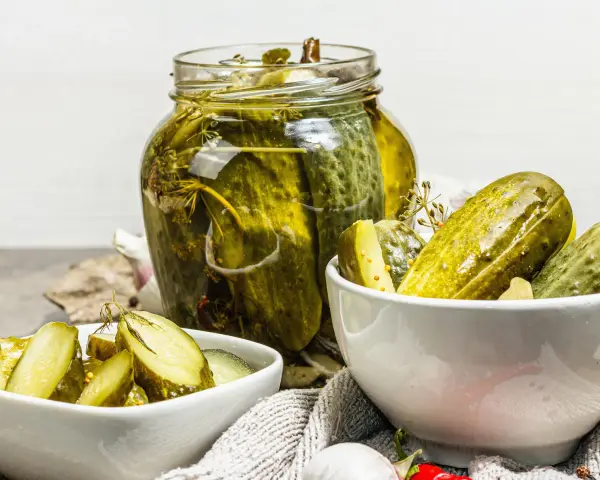 Cetrioli in agrodolce in un barattolo di vetro e in ciotole, con aglio e spezie.