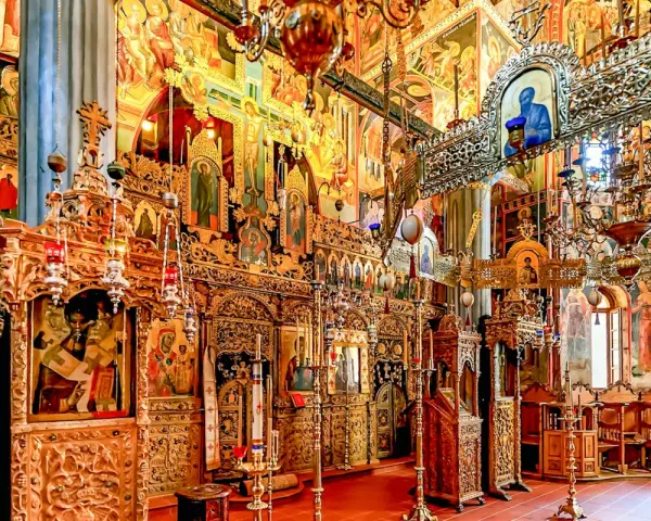 Interior of a richly decorated Orthodox church, showcasing ornate iconostasis, frescoes, and chandeliers, typical of many ancient christian monasteries.