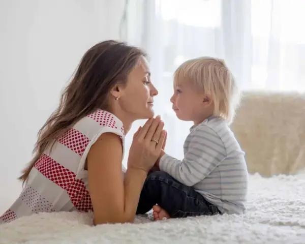 Mutter und Sohn beten zusammen. Sie halten ihre Hände gefaltet und schauen sich liebevoll an. Ein schöner Moment für kindergebete kurz.
