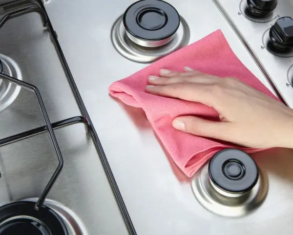 Mano con panno rosa lucida il piano cottura in acciaio.