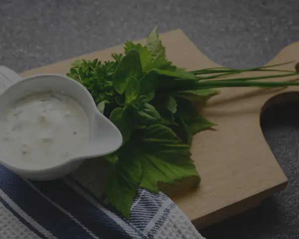 Sauce tartare maison crémeuse dans un ramequin blanc, accompagnée d'herbes fraîches sur une planche en bois.