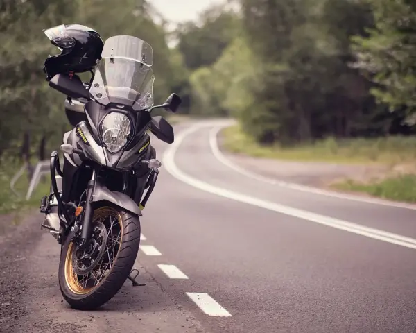 Moto pronta per avventurosi itinerari in moto su una strada tortuosa tra alberi. Casco appoggiato sul manubrio.