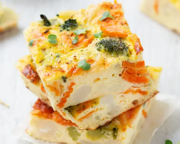 Fette di frittata al forno con verdure, broccoli e carote, guarnita con germogli freschi. Un piatto colorato e salutare.