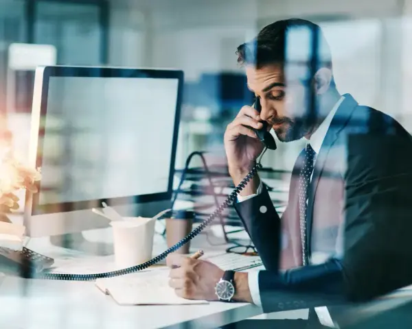 Biznesmen w garniturze rozmawia przez telefon, notując w zeszycie. Nawet w obliczu siły wyższej, praca wre.
