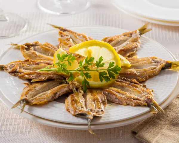 Piatto di alici alla scapece disposte a raggiera, guarnite con fette di limone e prezzemolo.