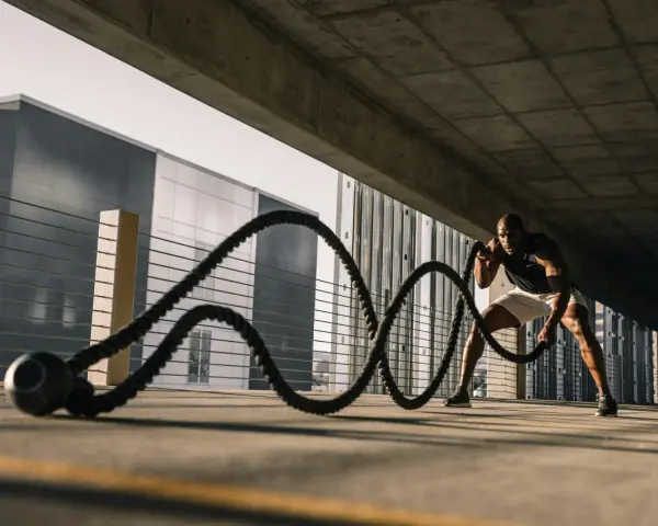 Un homme s'entraîne avec des cordes de bataille sous un pont. Il est concentré, ses muscles tendus. Les bienfaits de la glutamine pour la récupération sont essentiels pour ce type d'effort.