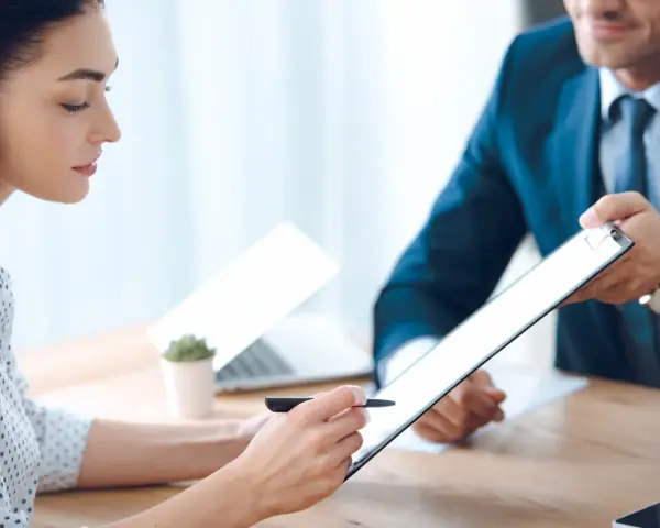 Kobieta podpisuje dokument na tablecie, mężczyzna w garniturze podaje jej go.