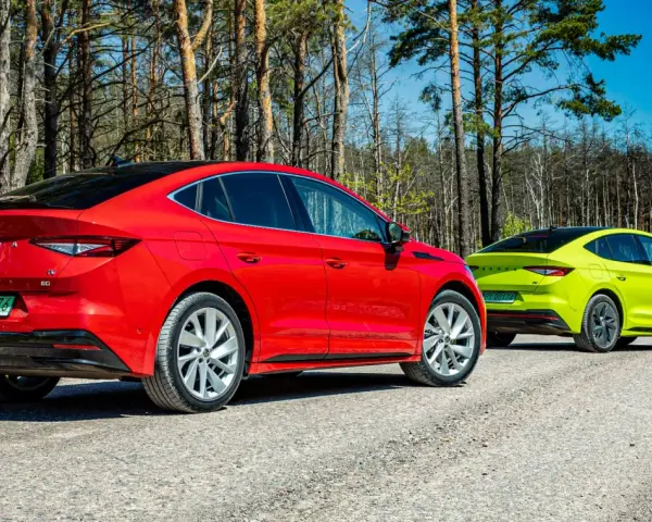 Dwa samochody Skoda Enyaq w kolorach czerwonym i limonkowym na leśnej drodze.