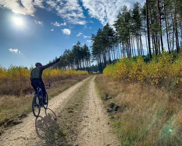 Rowerzysta cieszy się jazdą po szutrowej drodze wśród jesiennych drzew.