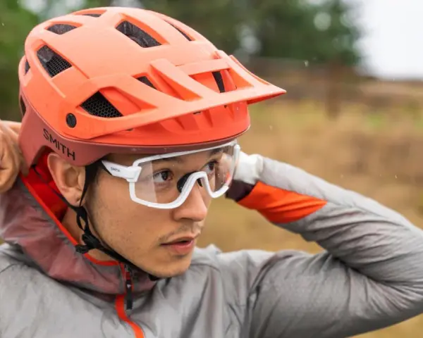 Uomo con casco da bici arancione e occhiali bianchi, mentre regola il casco. Utile per capire come misurare la testa per il casco.