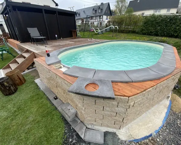 Ein Pool mit selbstgemachten Randsteinen, umgeben von Holz und Naturstein.