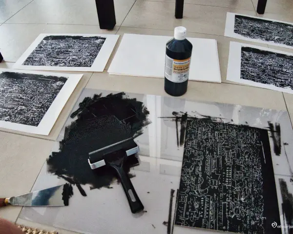 Na podłodze leży papier do linorytu, czarny tusz, wałek i kilka gotowych odbitek.
