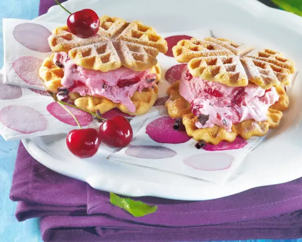 Zwei herzförmige Waffeln gefüllt mit Kirscheis und Schokostückchen, garniert mit frischen Kirschen. Ein süßer Genuss!