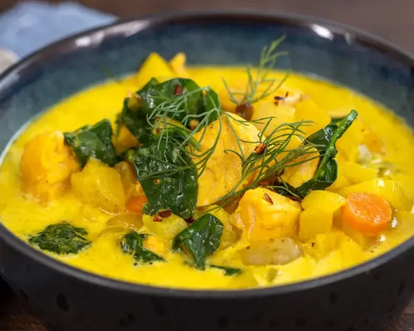 En skål med krämig fisksoppa saffran, fylld med fiskbitar, potatis, morötter och gröna blad, garnerad med dill.