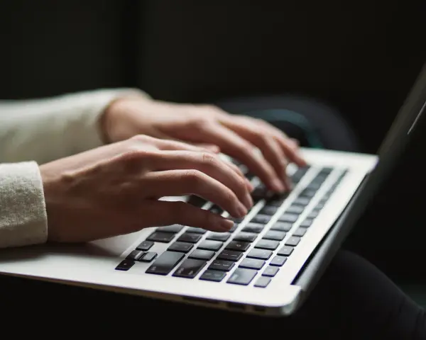 Dłonie piszą na laptopie. Ktoś przygotowuje wypowiedzenie umowy o pracę po angielsku, szukając wzoru.