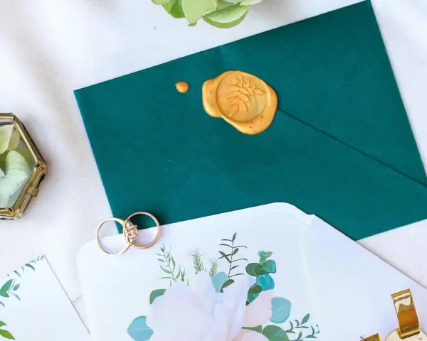 Elegancka koperta z pieczęcią, obrączki i zaproszenie. Zastanawiasz się, ile trzeba dać w kopercie na wesele?