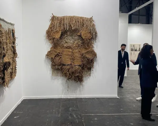 Exposición de arte contemporáneo con tapices texturizados y personas observando.