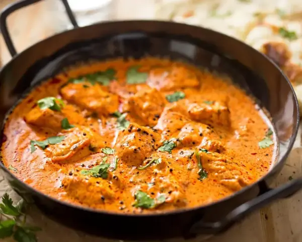 Aksamitny kurczak w sosie curry, udekorowany świeżą kolendrą, kusi aromatem. Obok widać kawałki chleba naan.