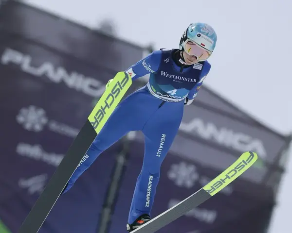 Skoczkini narciarska w locie, w niebieskim kombinezonie, z nartami Fischer. Planica.