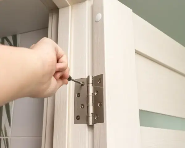 Dłoń dokręca śrubę zawiasu, montując drzwi ukryte w ścianie.