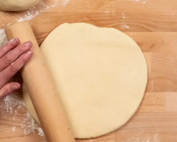 Hand rollt Teig auf Holzbrett aus. Vielleicht mit Dinkelmehl? Was ist Dinkelmehl?