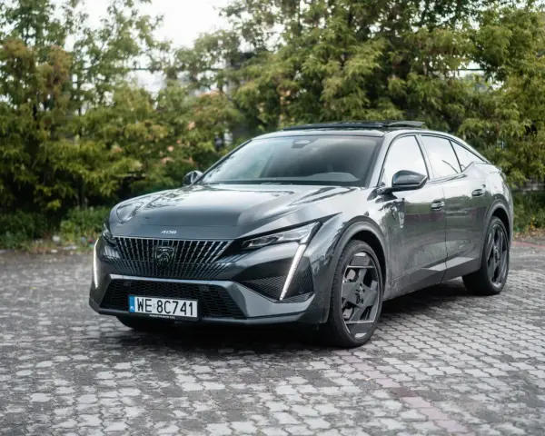 Nowy Peugeot 408 w ciemnoszarym kolorze prezentuje się elegancko na tle zieleni.