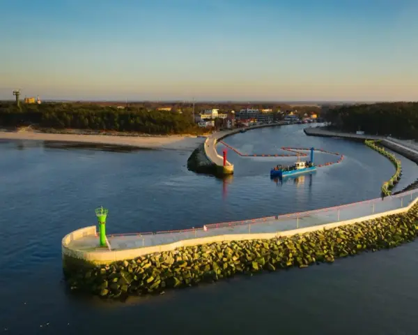 Port w Mrzeżynie z falochronami i latarniami morskimi. Widoczna łódź pogłębiarka. Mrzeżyno atrakcje dla miłośników morza.