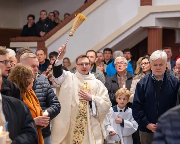 Kapłan błogosławi wiernych podczas liturgii Wielkiej Soboty, unosząc kropidło. W tłumie widać ludzi z zapalonymi świecami.